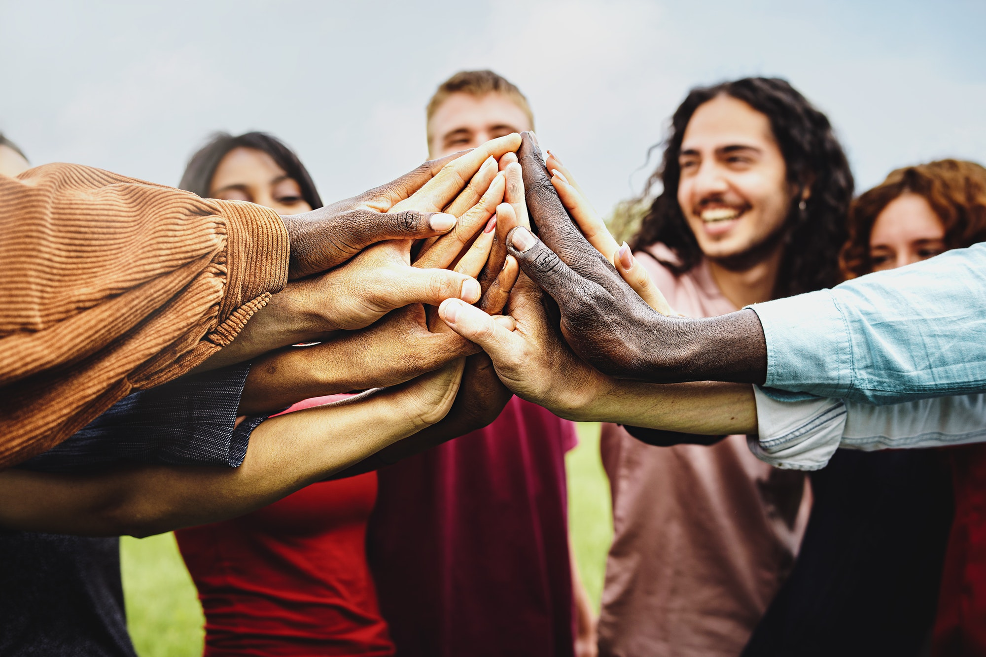 A diverse group of hands reaching towards each other in a gesture of unity and collaboration, with happy individuals in the background.